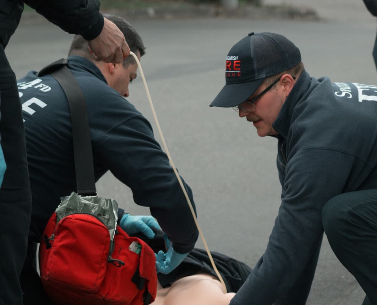 Emergency responders practice trauma care on a training dummy, using medical tape and gear during a simulated disaster response drill.